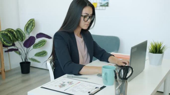 美丽的亚洲上班族在工作场所用笔记本电脑打字和喝咖啡的慢动作