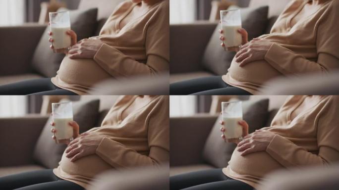孕妇正在喝牛奶，轻轻地抚摸她的肚子