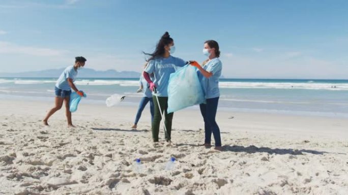 穿着志愿者t恤和口罩的多元化妇女从海滩上捡垃圾