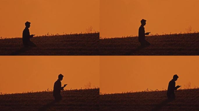 SLO MO Farmer在橙色的天空下走过麦田时使用电话