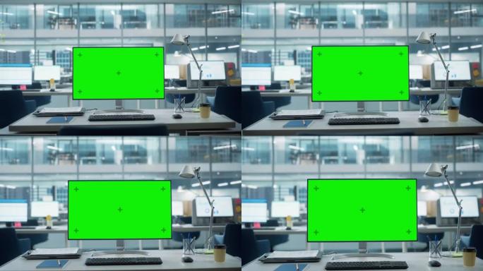 台式电脑显示器，带有模拟绿屏色度键显示屏，站在现代商务办公室的桌子上。在带有大城市办公室的背景玻璃墙