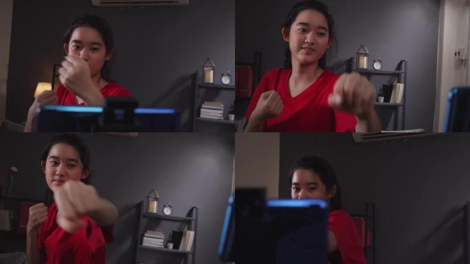 迷人的亚洲少年在家里的客厅在她的智能手机中观看和做拳击在线直播课。她在应用程序中使用手机进行训练练习