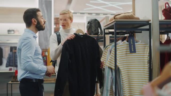 英俊的男性顾客在服装店购物，零售助理提供建议。时尚商店里的人多样化，选择时尚的衣服，具有可持续设计的