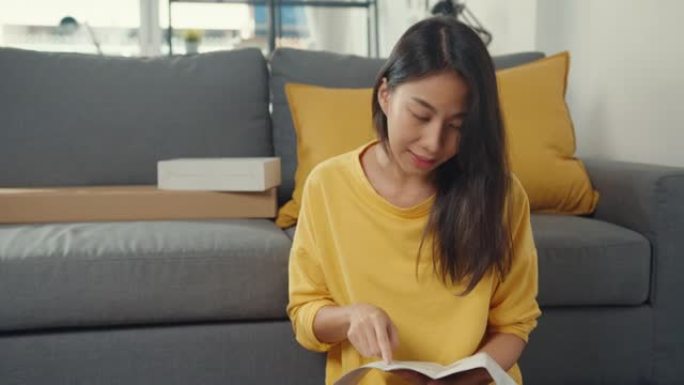 快乐的亚洲年轻女子打开包装盒并阅读说明组装新家具装饰房屋构建表。