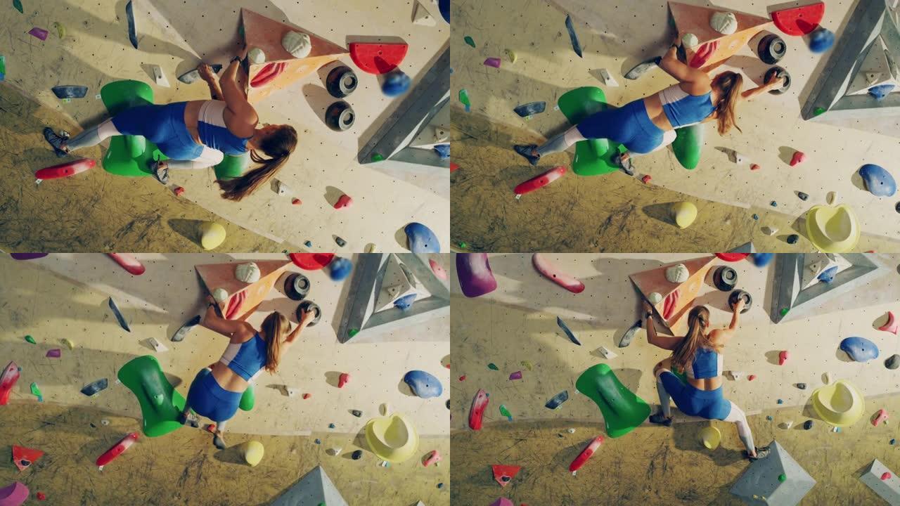 运动女攀岩者在健身房的抱石墙上练习单人攀岩。女性在室内健身设施锻炼，为健康的生活方式训练做极限运动。