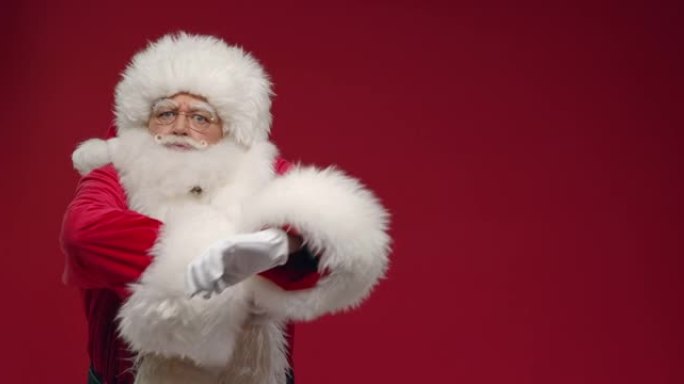一个脾气暴躁的圣诞老人用食指责骂观众，交叉双臂，站在红底