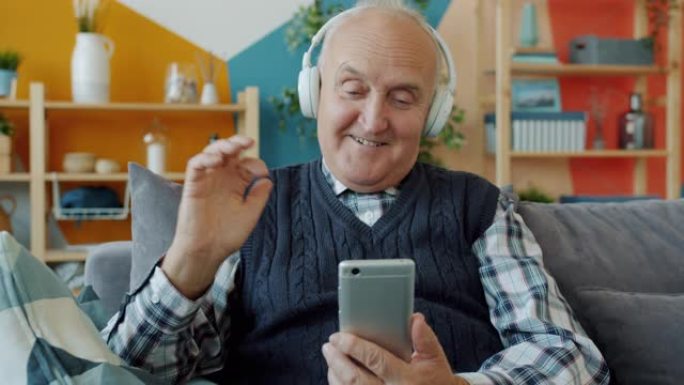 老人在家里用智能手机戴着耳机听音乐放松