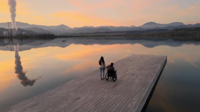 女人与丈夫在湖码头上的轮椅上散步