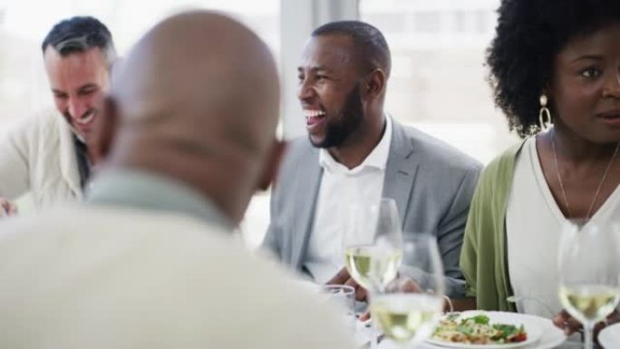 一群不同的人在吃饭时一起开玩笑和大笑。微笑的朋友坐在里面享受美味的午餐或晚餐。享受食物并感到快乐和社