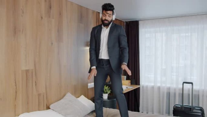 快乐的中东男子戴着耳机在酒店房间的床上跳舞