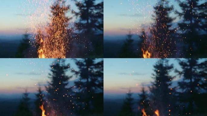 明亮的火花从火中飞来，漂浮在空中。篝火、野外露营、徒步旅行。背景上的山脉、树木和日落天空。慢动作，4