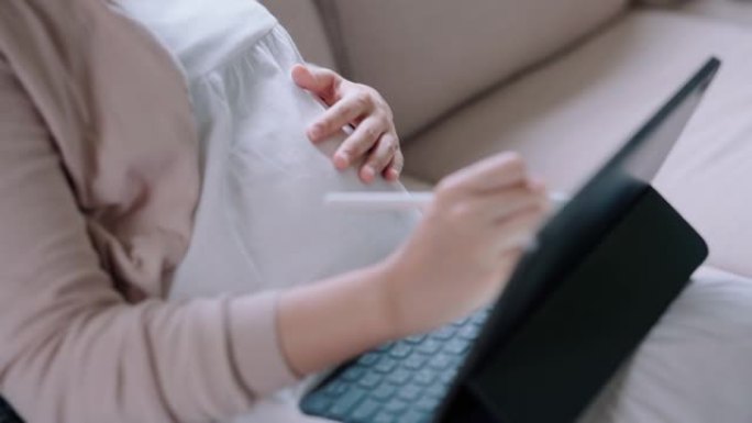 在数字平板电脑上工作的年轻孕妇。