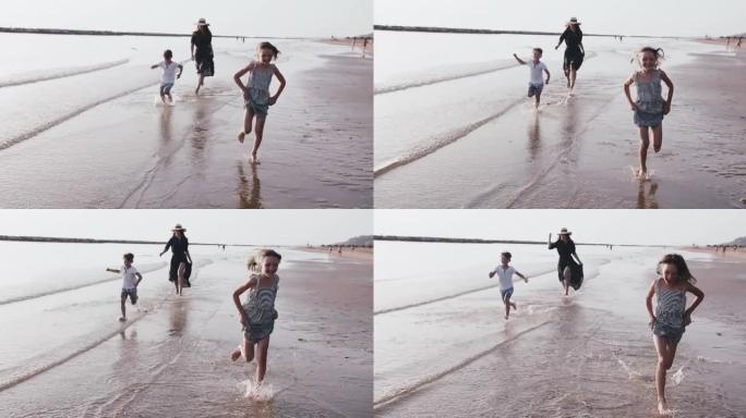 爱情和家庭度假，两个快乐的孩子在日出海滩水上与年轻的母亲慢动作一起玩耍。