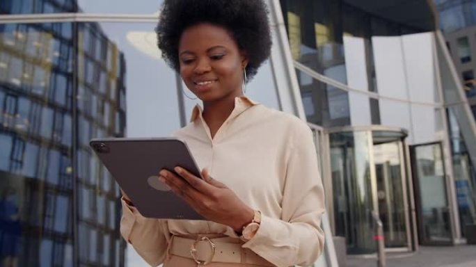 一位穿着米色衬衫的年轻黑皮肤卷发商务女士用平板电脑微笑着