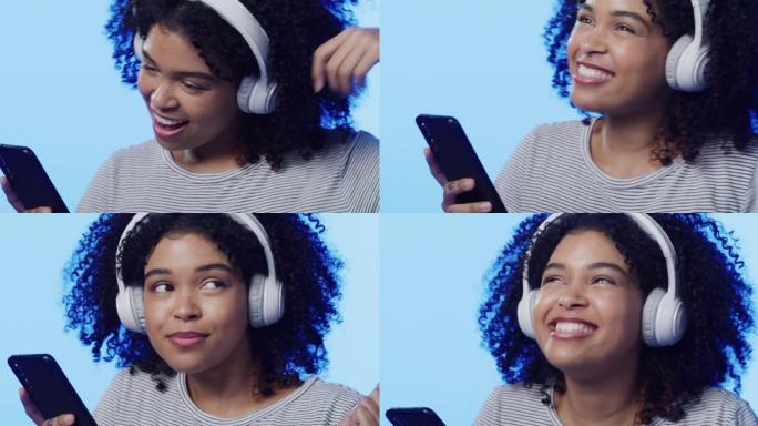 4k视频片段，一个美丽的年轻女子戴着耳机使用手机并在蓝色背景下跳舞