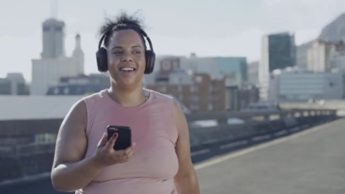 加大码的女人用无线蓝牙耳机听音乐，锻炼身体，用手机追踪城市的体重减轻。胖乎乎的活跃女人开始常规户外锻