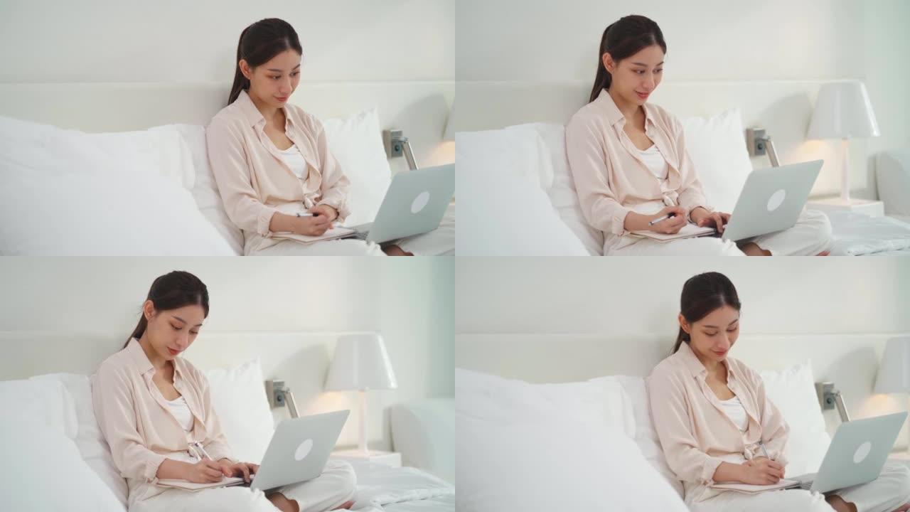亚洲女商人在床上写记事本和使用技术笔记本电脑进行在线学习