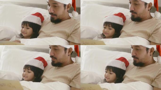 亚洲父亲正在卧室里和女儿一起读圣诞节童话。