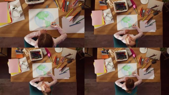 俯视图: 小女孩画我们美丽的地球，抬头微笑。有才华的孩子将我们的家园想象成一个快乐的地方，拥有干净、