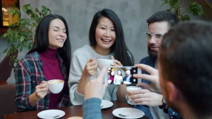 快乐的人们在咖啡馆里碰杯庆祝，而男人用智能手机相机拍照