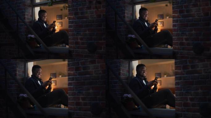 非裔美国人晚上坐在布鲁克林风格的褐砂石房屋的窗台上时使用智能手机。黑人男性浏览社交媒体约会应用程序人