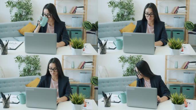 亚洲女企业家使用笔记本电脑在家打字喝咖啡的慢动作
