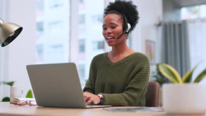 自信的黑人女性呼叫中心代理在办公室的笔记本电脑上工作时戴着耳机说话。自信的非洲裔美国顾问为客户服务和