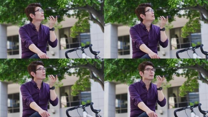 亚洲男子坐在公司公园附近时，骑着自行车在智能手机上聊天