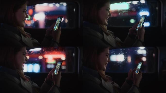 快乐的女性晚上坐出租车后座回家。美丽的女人乘客在智能手机上玩街机视频游戏，而在城市街道上的一辆有工作