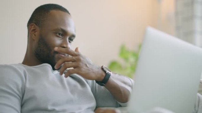 非洲民族的快乐年轻人在家里用笔记本电脑工作，而早上坐在沙发上在家放松。现代技术概念的人。