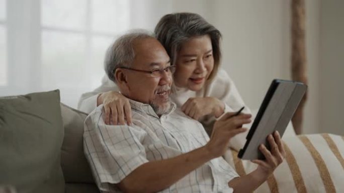 亚洲老年夫妇在家里一起使用数字平板电脑
