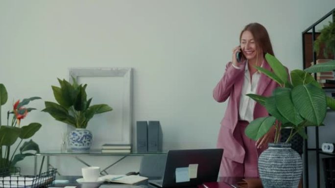 工作忙。快乐成功的30多岁金发老板在办公室工作的女商人使用笔记本电脑，通过手机交谈。