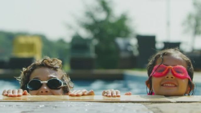两个戴着游泳镜的孩子的肖像在度假时看着室外游泳池的边缘-慢动作拍摄