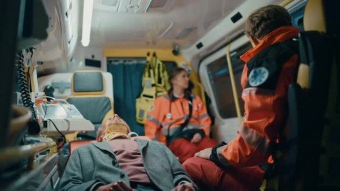 女性和男性专业急救护理人员在救护车上受伤的年轻男性患者戴着颈圈。穿着制服的急救助理坐在去医院的路上。