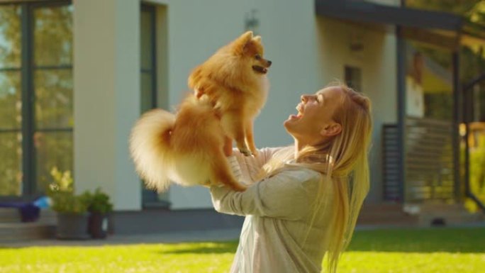 美丽的女人在户外草坪上野餐时抱着她最喜欢的博美犬。她抚摸和拥抱她的小狗。田园诗般的避暑别墅。慢动作