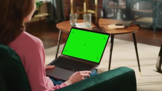 女性进行视频通话，手持带有绿屏模拟显示的笔记本电脑。在家工作时，专家会赶上同事。女人与朋友和家人交谈