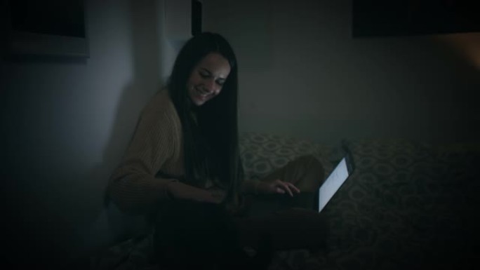 女人在家里的床上深夜用笔记本电脑抚摸她的猫