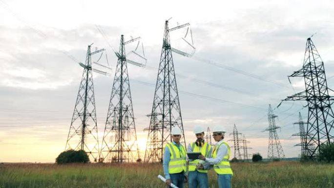 三名电工在日落时观察大型发电厂