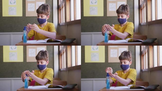 男孩坐在学校的桌子上戴着口罩消毒双手
