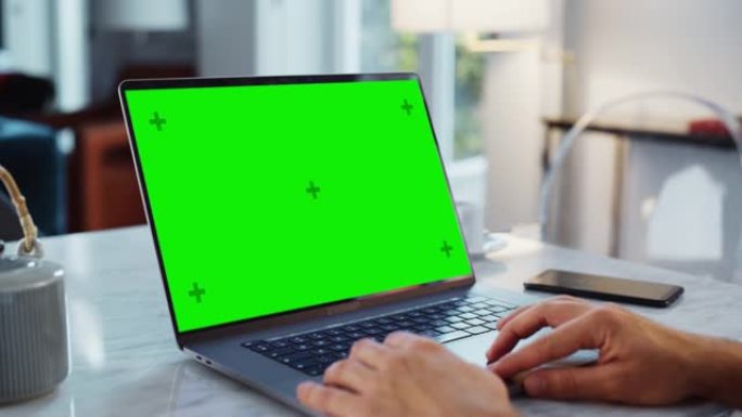 笔记本电脑上的绿屏模拟显示。使用触摸板，滚动内容，在现代家庭中近距离工作。智能手机位于计算机旁边。
