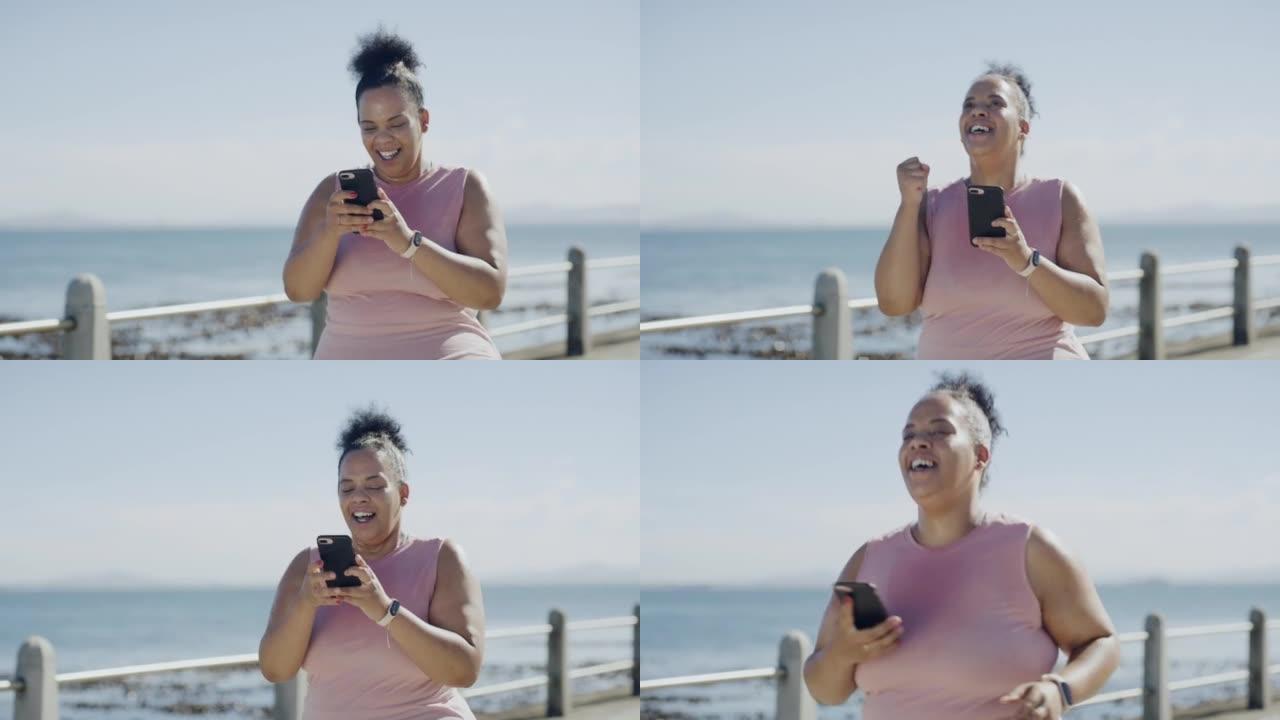 一位年轻的大码女士庆祝减肥之旅，并专注于健康，有氧运动，健身和精力。幸福的女人在海滩上的手机上安装了