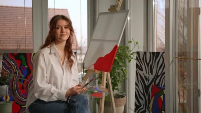 一位年轻女画家的SLO MO肖像在她的工作室摆姿势时微笑
