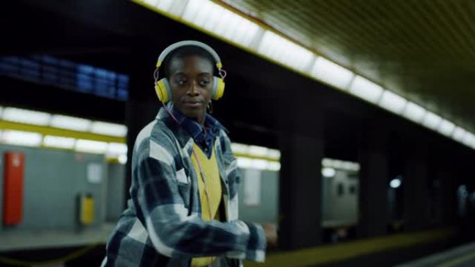 年轻时尚的黑人妇女，戴着黄色耳机，在空荡荡的地铁站独自听音乐和跳舞。充满活力的自信年轻女性跟随节拍并