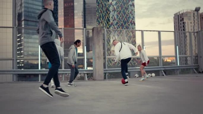 年轻时尚的人在现代城市摩天大楼周围的屋顶上踢足球。年轻的足球运动员盘带，炫耀技巧和躲避对手。跟踪手持