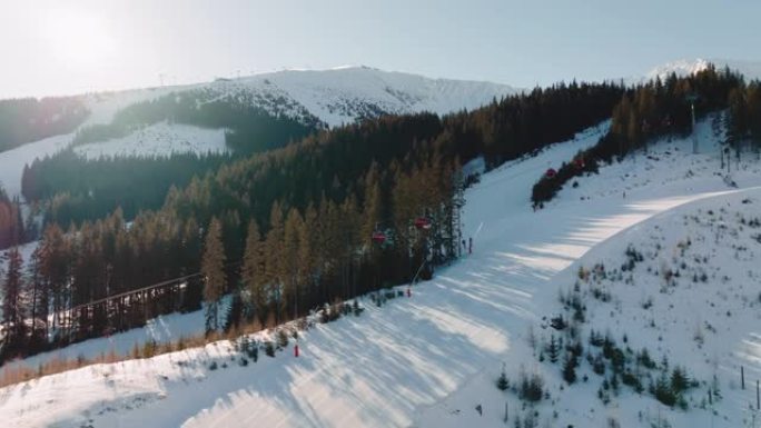 冬季娱乐无人机飞过滑雪缆车，在阳光明媚的雪山背景下，在美丽的斜坡小径上工作。