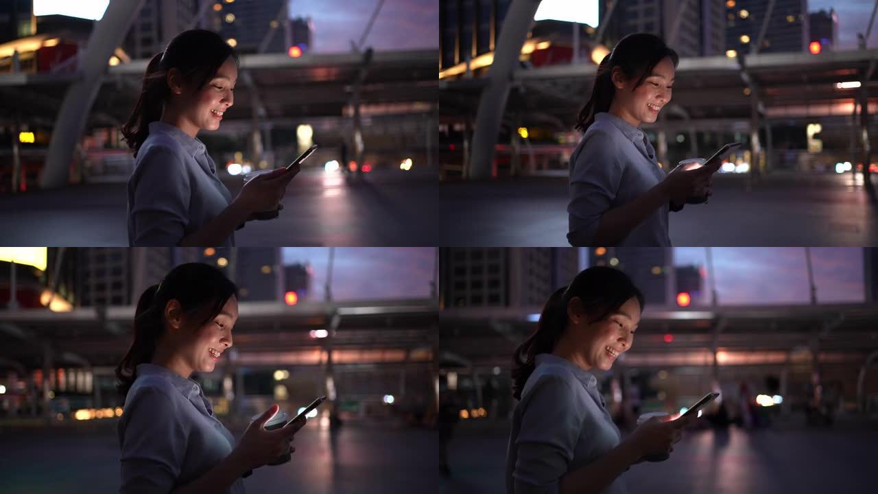 年轻的亚洲女商人下班后晚上在城市散步时使用智能手机发送短信