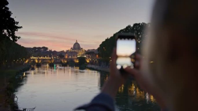 一名女性在黄昏时用智能手机拍下了圣天使桥和圣彼得大教堂的照片