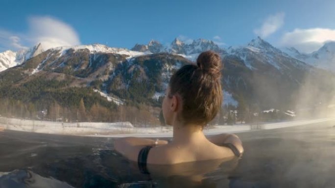在山区度假期间，一名年轻女性正在豪华健康中心的热水浴管中享受和放松。假期和福祉的概念。