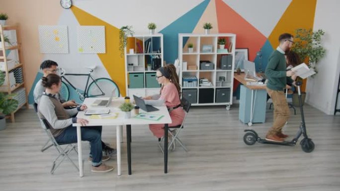商业团队在创意办公室工作，而家伙在室内骑踏板车玩得开心