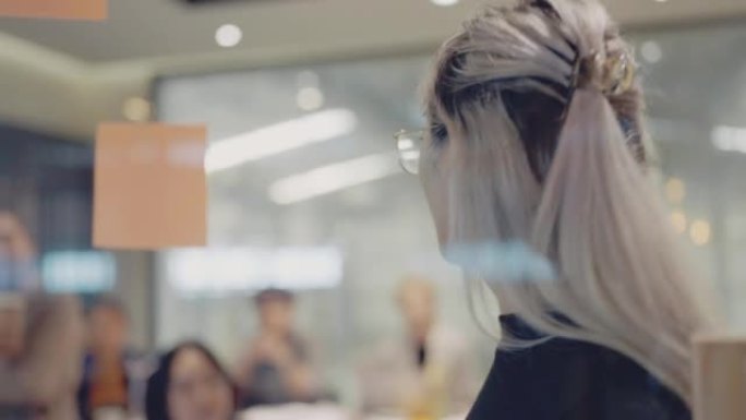 年轻的亚洲女企业家在会议室的玻璃墙上攻击便签。